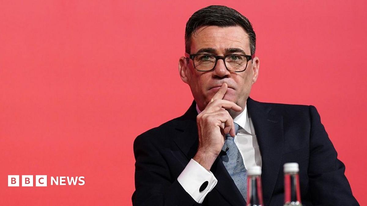 Andy Burnham looks pensive while sitting down with a red background